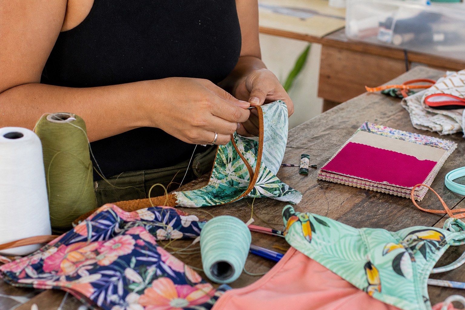 Artisan hands hand-sewing swimwear fabric at a workshop table